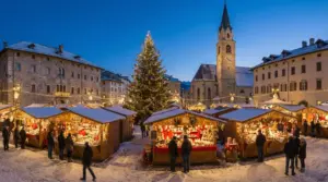 Bancarelle illuminate in un mercatino di Natale con persone e un grande albero decorato al centro della piazza